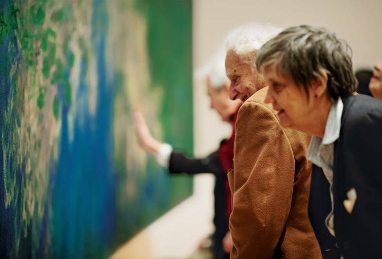 Photo: Jason Brownrigg ©️ 2024 The Museum of Modern Art, NY. Image description: Side view of a group of adults looking closely at a blue and green abstract painting that fills the wall.