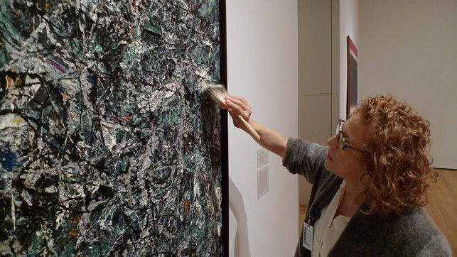 Conservators routinely inspect and dust the works on view in the galleries. Here, paintings conservator Anny Aviram dusts Jackson Pollock’s Full Fathom Five (1947)