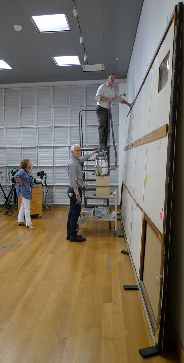Paintings conservator Michael Duffy, on ladder, removes loose dust from the top edge of One: Number 31, 1950, and the first panels of the painting’s protective backing are removed