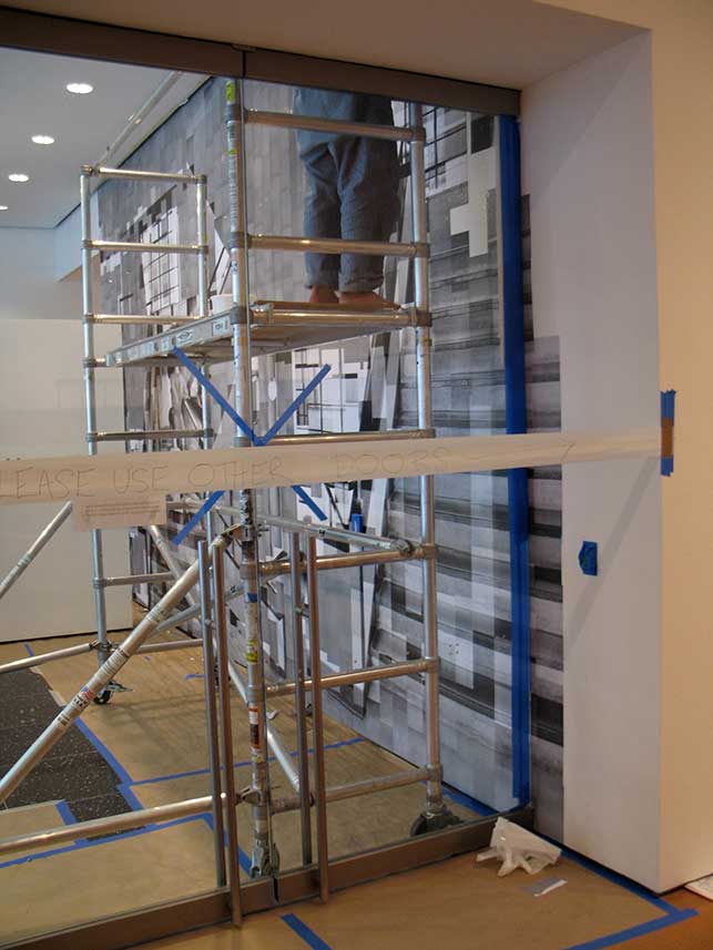 : Katharina Gaenssler at work, October 29, 2015. Covering the area meant going all the way to the ceiling with the photo-mural, and into the doorway of the Robert B. Menschel Gallery. Photo: Kristen Gaylord