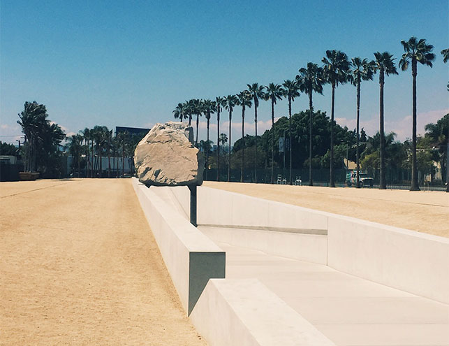A view of the LACMA exterior. Shown: Michael Heizer. Levitated Mass. 2012. Diorite granite and concrete, 35 × 456 × 21 2/3' (10.67 × 138.98 × 6.6 m). Purchased with funds provided by Jane and Terry Semel, Bobby Kotick, Carole Bayer Sager and Bob Daly, Beth and Joshua Friedman, Steve Tisch Family Foundation, Elaine Wynn, Linda, Bobby, and Brian Daly, Richard Merkin, MD, and the Mohn Family Foundation, and dedicated by LACMA to the memory of Nancy Daly. Transportation made possible by Hanjin Shipping Holdings Co., Ltd. (M.2011.35). Photo: Annikka Olsen